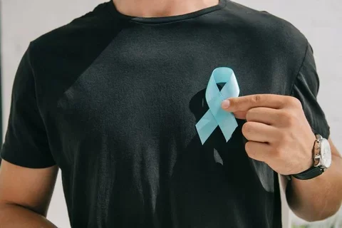 a man in a black shirt is holding a light blue ribbon symbolizing prostate cancer