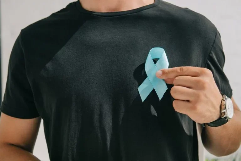 a man in a black shirt is holding a light blue ribbon symbolizing prostate cancer