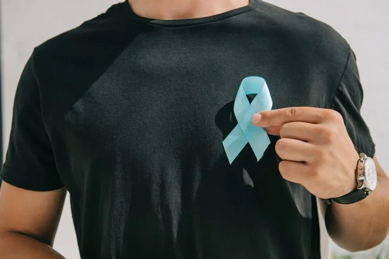 a man in a black shirt is holding a light blue ribbon symbolizing prostate cancer