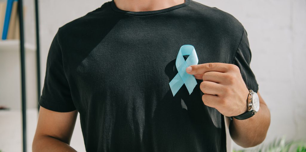partial view of man in black t-shirt holding blue awareness ribbon